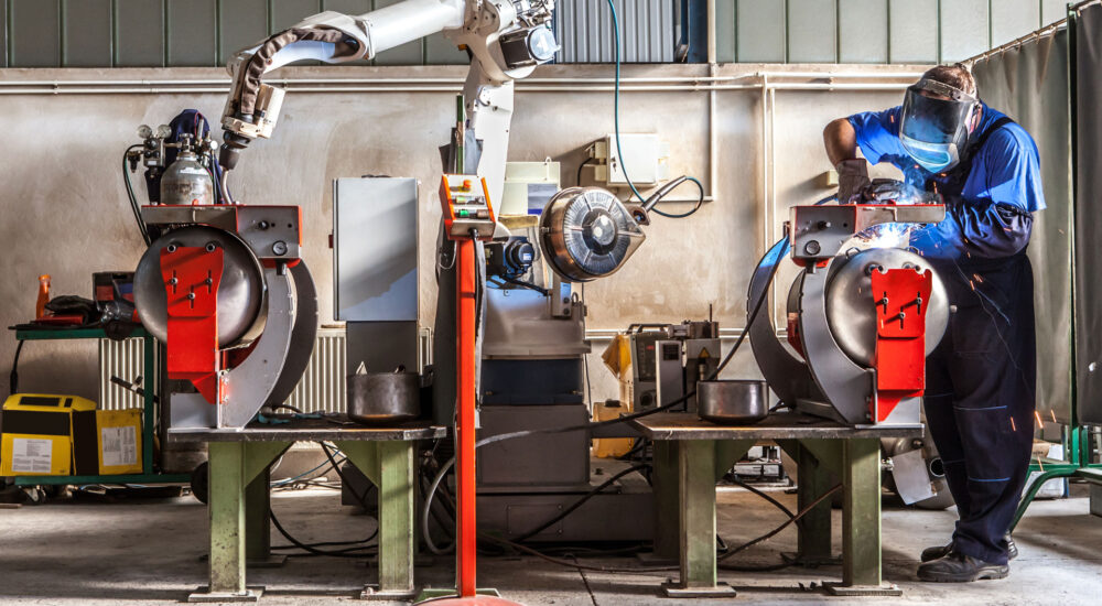 The mechanical performs welds metal components assisted by a worker.